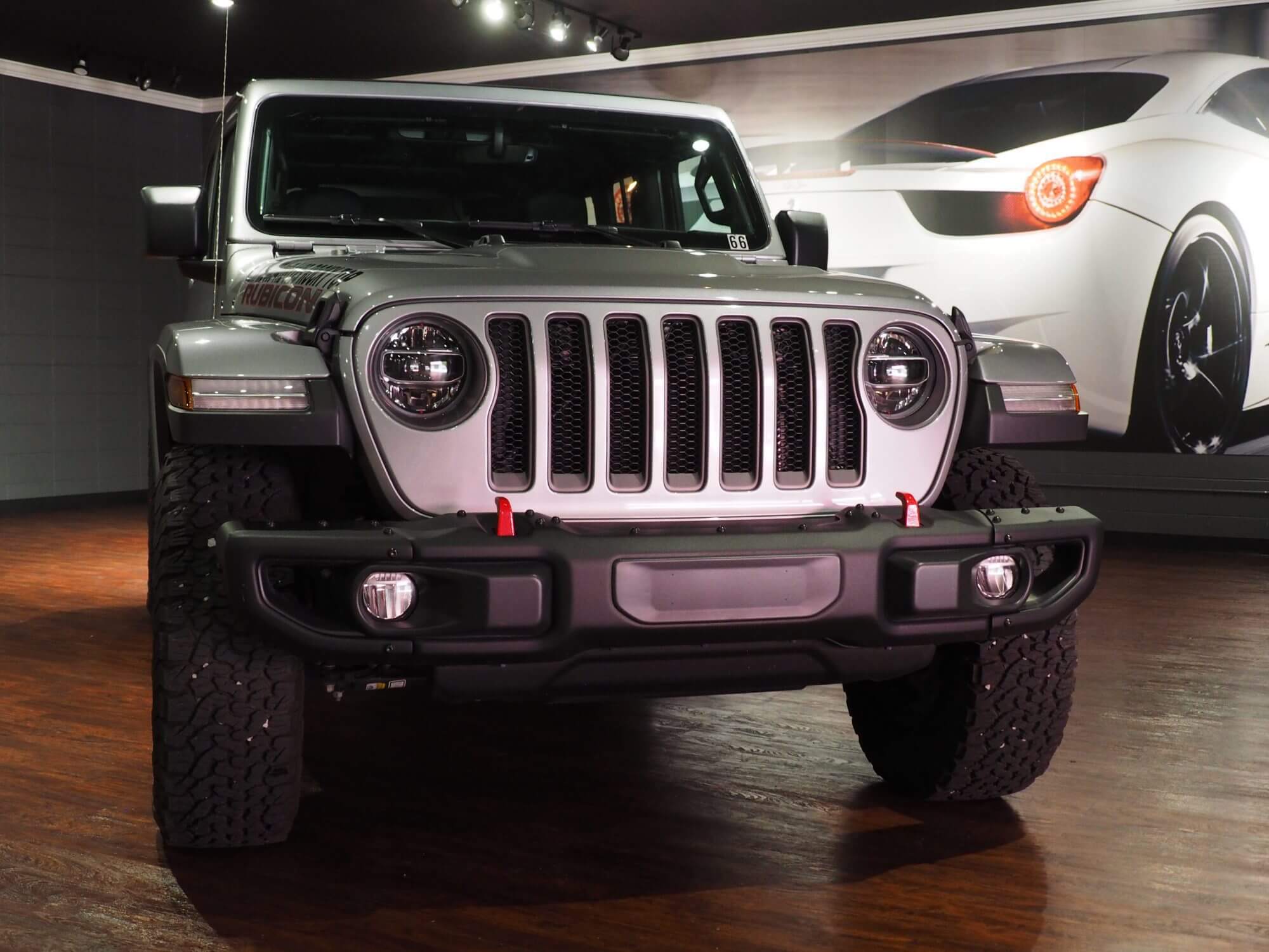 Rubicon Jeep showcased on hardwood floor with lighting and sports car backdrop